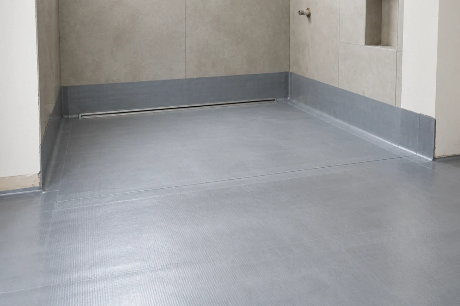 Continuous waterproofing across a curbless shower threshold with a rear linear drain.